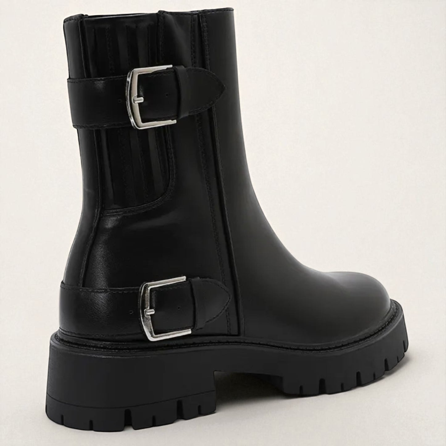 Black boot with silver buckles on a light gray background